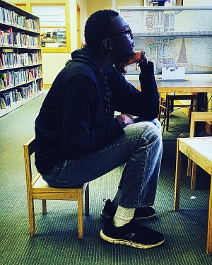 male student sitting in small chair brainstorming essay ideas.