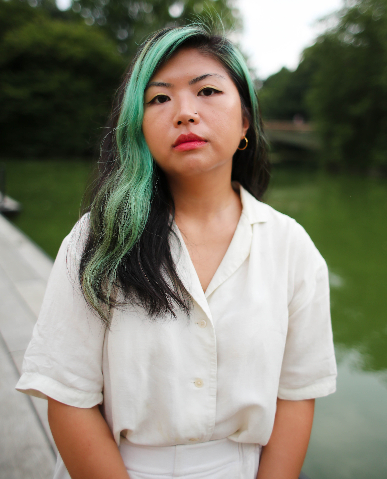 Author Gina Chung wearing a white short and a green dyed stripe down one side of her parted long black hair